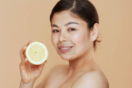Photo for Portrait of young asian female with lemon isolated on beige background. - Royalty Free Image