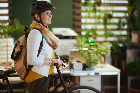 Photo for Smiling elegant business woman in bike helmet with bicycle and backpack in modern eco office. - Royalty Free Image