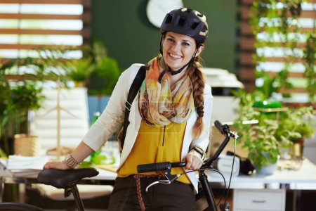 Foto de Feliz mujer de negocios con estilo en casco de bicicleta con bicicleta en eco oficina moderna. - Imagen libre de derechos