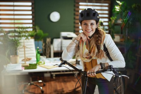 Foto de Portrait of happy stylish middle aged business woman in bike helmet with bike in modern eco office. - Imagen libre de derechos
