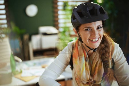 Foto de Retrato de elegante mujer de negocios de 40 años sonriente en casco de bicicleta en eco oficina moderna. - Imagen libre de derechos