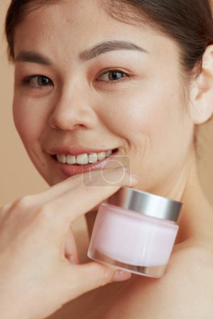 Foto de Retrato de mujer moderna con frasco de crema facial sobre fondo beige. - Imagen libre de derechos