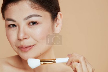 Téléchargez les photos : Portrait de femme moderne avec pinceau de maquillage sur fond beige. - en image libre de droit