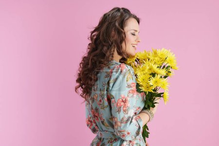 Photo for Happy stylish woman with long wavy brunette hair with yellow chrysanthemums flowers isolated on pink background. - Royalty Free Image