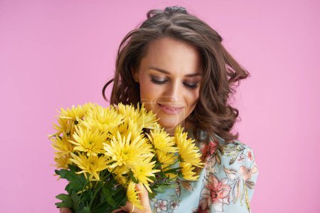Foto de Mujer joven y relajada en vestido floral con flores de crisantemos amarillos aisladas en rosa. - Imagen libre de derechos