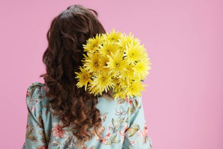 Photo for Seen from behind woman in floral dress with yellow chrysanthemums flowers against pink background. - Royalty Free Image