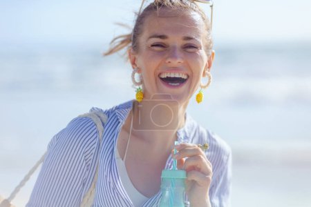Téléchargez les photos : Portrait de femme élégante souriante avec boisson à la plage. - en image libre de droit