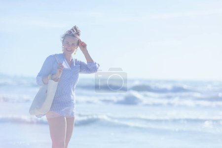 Téléchargez les photos : Heureuse femme élégante de 40 ans avec sac de paille blanche à la plage. - en image libre de droit