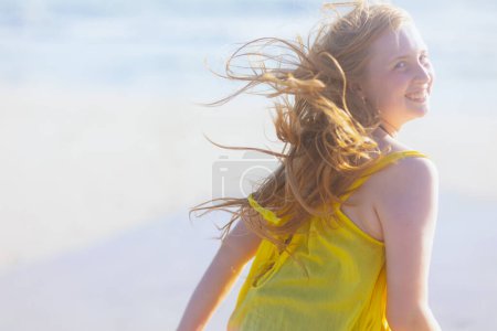 Foto de Sonriente adolescente moderno en la playa en vestido colorido divertirse. - Imagen libre de derechos