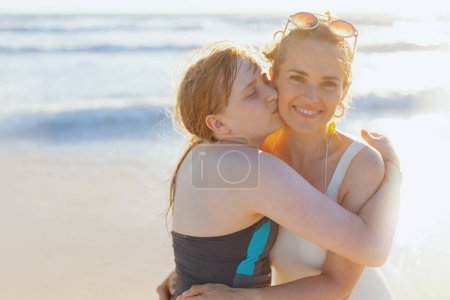 Photo for Portrait of smiling modern mother and teenage daughter at the beach in swimsuit hugging. - Royalty Free Image