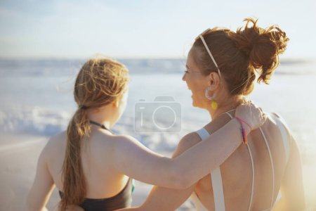 Foto de Visto desde atrás elegante madre e hijo en la playa en traje de baño divertirse. - Imagen libre de derechos