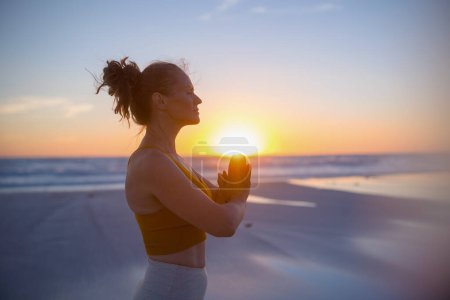 Téléchargez les photos : Femme de forme détendue joggeuse en vêtements de sport à la plage au coucher du soleil méditant. - en image libre de droit