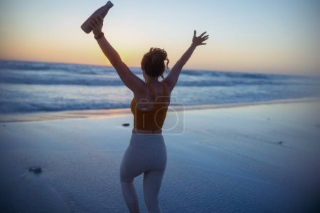 Téléchargez les photos : Vu de derrière femme en forme joggeuse en vêtements de sport avec bouteille d'eau se réjouissant. - en image libre de droit