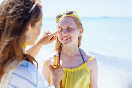 Photo for Happy modern mother and teenage daughter at the beach applying spf. - Royalty Free Image
