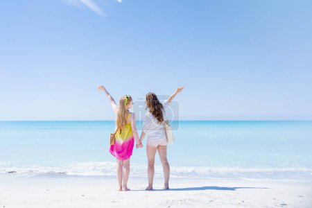 Foto de Visto desde atrás madre moderna e hija adolescente en la playa regocijándose. - Imagen libre de derechos