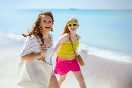 Foto de Sonriente elegante madre e hija adolescente en la playa caminando. - Imagen libre de derechos
