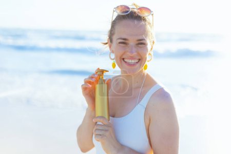 Foto de Retrato de mujer elegante feliz en ropa de playa blanca en la playa usando spf. - Imagen libre de derechos