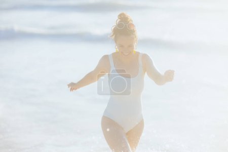 Téléchargez les photos : Souriant élégant femelle en maillot de bain blanc à la plage avoir du plaisir. - en image libre de droit
