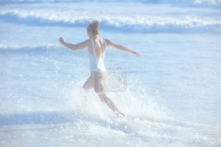 Foto de Visto desde atrás mujer moderna en ropa de playa blanca en la playa divertirse. - Imagen libre de derechos