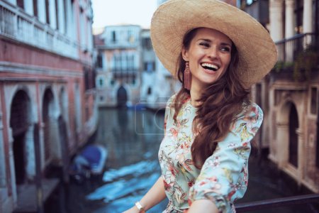 Foto de Mujer de moda feliz en vestido floral con sombrero explorar atracciones en Venecia, Italia. - Imagen libre de derechos