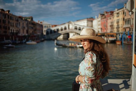 Photo for Modern solo traveller woman in floral dress with hat on embankment near Rialto Bridge in Venice, Italy. - Royalty Free Image