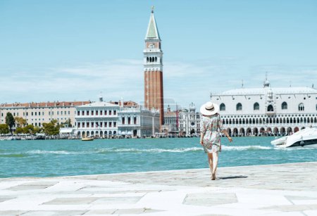 Von hinten gesehen trendige Frau in floralem Kleid mit Hut erkundet Sehenswürdigkeiten auf der Insel San Giorgio Maggiore.