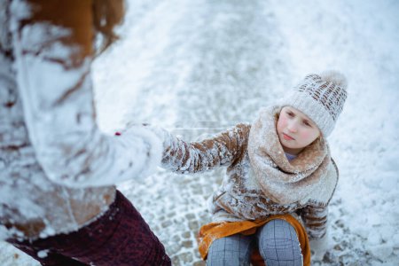 Photo for Mother helping daughter getting up after falling outdoors in the city park in winter. - Royalty Free Image