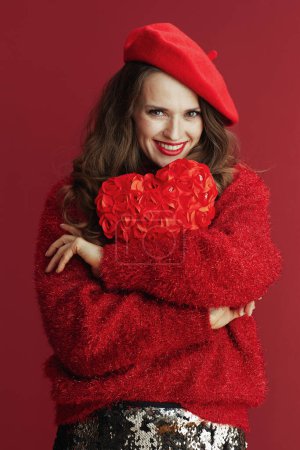 Téléchargez les photos : Joyeux Valentin. souriant élégant femme d'âge moyen en pull rouge et béret avec coeur rouge étreignant coeur rouge. - en image libre de droit