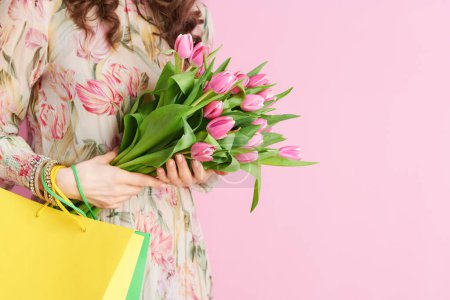 Téléchargez les photos : Gros plan sur femme avec bouquet de tulipes et sacs à provisions isolés sur rose. - en image libre de droit