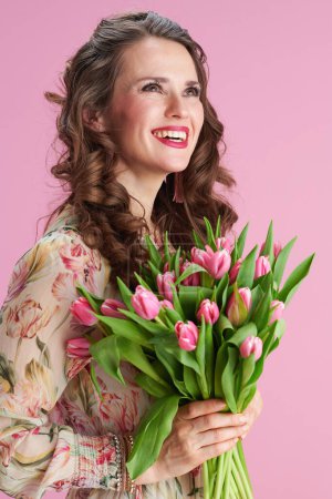 Photo for Smiling stylish woman with long wavy brunette hair with tulips bouquet against pink background. - Royalty Free Image