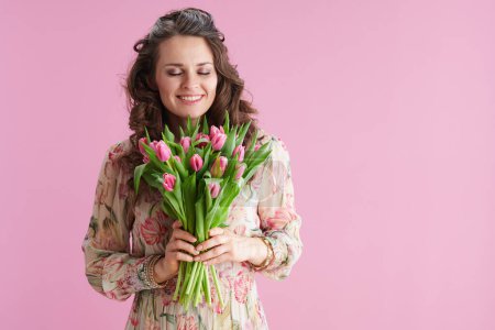 happy modern woman with long wavy brunette hair with tulips bouquet isolated on pink background.