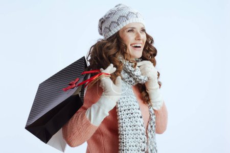 Téléchargez les photos : Bonjour l'hiver. Femme souriante tendance en pull, mitaines, chapeau et écharpe sur fond blanc avec des sacs à provisions. - en image libre de droit