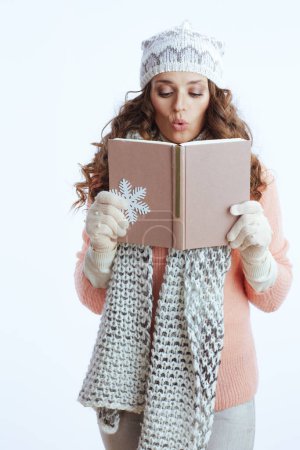 Téléchargez les photos : Bonjour l'hiver. surpris femme à la mode en pull, mitaines, chapeau et écharpe avec flocon de neige et livre isolé sur blanc. - en image libre de droit
