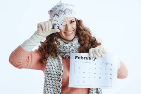 Bonjour l'hiver. heureuse femme à la mode en pull, mitaines, chapeau et écharpe isolé sur fond blanc avec calendrier février et flocon de neige.