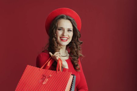 Photo for Happy Valentine. smiling stylish woman in red dress and beret with shopping bags isolated on red. - Royalty Free Image