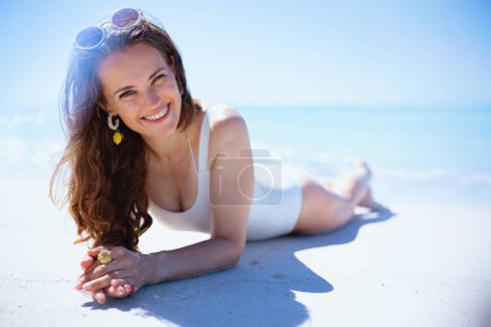 Foto de Retrato de mujer elegante feliz en traje de baño blanco que pone en la playa. - Imagen libre de derechos