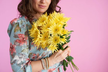 Photo for Closeup on middle aged woman with long wavy brunette hair with yellow chrysanthemums flowers isolated on pink background. - Royalty Free Image