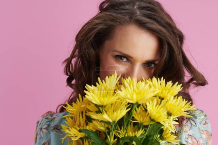 Photo for Happy modern 40 years old woman in floral dress with yellow chrysanthemums flowers isolated on pink. - Royalty Free Image
