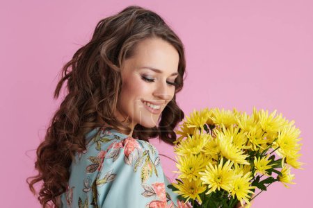 Téléchargez les photos : Heureuse élégante femelle en robe florale avec des fleurs de chrysanthèmes jaunes isolées sur rose. - en image libre de droit