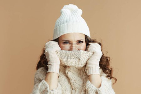 Photo for Hello winter. stylish middle aged woman in beige sweater, mittens and hat wrapped in a collar isolated on beige. - Royalty Free Image