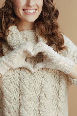 Photo for Hello winter. Closeup on happy middle aged woman in beige sweater, mittens and hat showing heart shaped hands against beige background. - Royalty Free Image