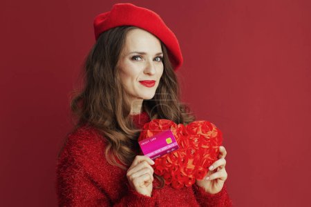Téléchargez les photos : Joyeux Valentin. femme d'âge moyen moderne en pull rouge et béret avec coeur rouge et carte de crédit. - en image libre de droit