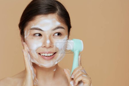 Téléchargez les photos : Jeune femme avec masseur lavage visage sur fond beige. - en image libre de droit