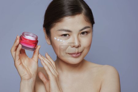 Téléchargez les photos : Jeune femme avec pot de crème faciale et crème faciale sur le visage sur fond bleu. - en image libre de droit