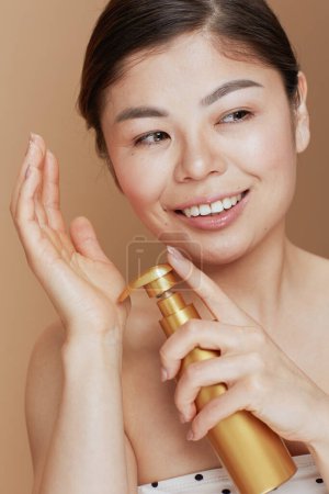 Photo for Modern asian female with self tanning mousse isolated on beige background. - Royalty Free Image