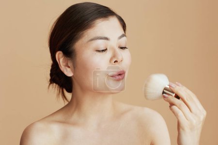 Téléchargez les photos : Femme asiatique moderne avec brosse de maquillage isolé sur fond beige. - en image libre de droit
