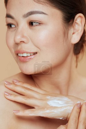 Téléchargez les photos : Portrait de femme moderne avec crème pour les mains isolée sur fond beige. - en image libre de droit