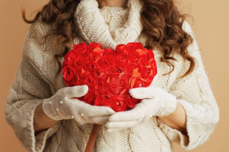 Téléchargez les photos : Hello winter. Closeup on woman in beige sweater, mittens and hat against beige background with red heart. - en image libre de droit