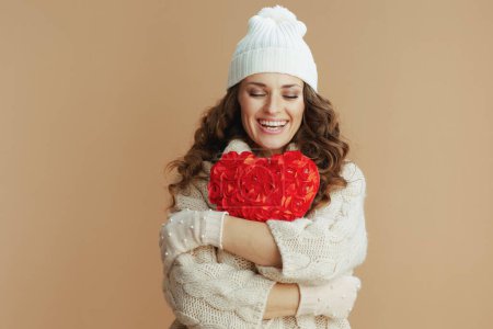 Téléchargez les photos : Hello winter. happy modern woman in beige sweater, mittens and hat against beige background with red heart. - en image libre de droit