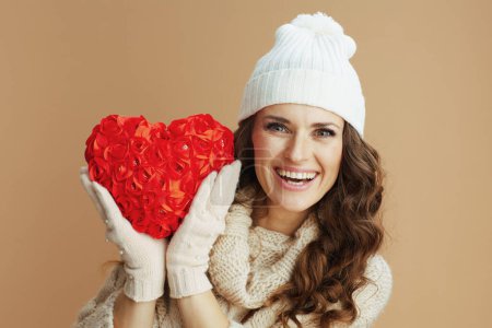 Photo for Hello winter. Portrait of happy modern middle aged woman in beige sweater, mittens and hat with red heart isolated on beige. - Royalty Free Image